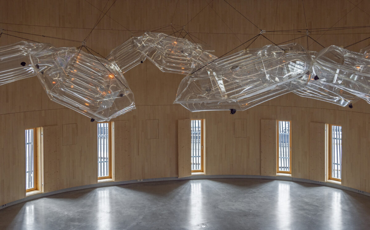 Veranstaltungsarena im Ellipsum mit natürlichem Tageslicht durch große Holzfenster – nachhaltige Architektur und warme Atmosphäre
